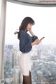 A woman standing in front of a window looking at her phone.