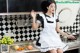 A woman in a black and white apron sitting on a kitchen counter.