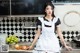 A woman in a maid outfit posing in a kitchen.