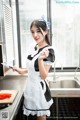 A woman in a maid outfit holding a knife in a kitchen.