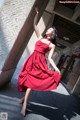 A woman in a red dress leaning against a wall.