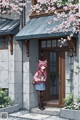 A girl standing in front of a building with cherry blossoms.