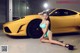 A woman in a blue bikini sitting next to a yellow sports car.