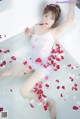 A woman in a bathtub with rose petals floating in it.