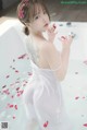 A woman in a white dress sitting in a bathtub with rose petals.