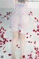 A woman in a white dress is standing in a bathtub filled with rose petals.