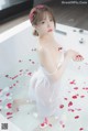 A woman in a white dress sitting in a bathtub with rose petals.