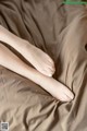 A woman's bare feet on a bed covered in brown sheets.