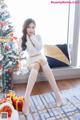 A woman sitting on a window sill next to a Christmas tree.