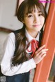 A young woman in a school uniform leaning against a window.