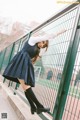 A woman in a school uniform leaning against a fence.