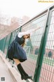 A woman in a school uniform leaning against a fence.