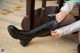 A woman sitting on the floor tying up a pair of boots.