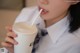 A woman in a school uniform drinking from a cup with a straw.