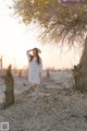 A woman in a white dress standing next to a tree.