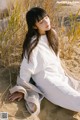 A woman in a white dress sitting in the sand.