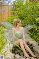 A woman in a green dress sitting on a rock in a garden.