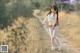 A woman walking down a dirt road in a field.