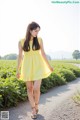 A woman in a yellow dress walking down a dirt road.