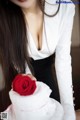 A woman in a white shirt holding a red rose.