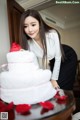 A woman standing next to a white cake with red roses on it.