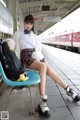 A woman sitting on a blue chair at a train station.