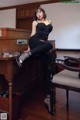 A woman sitting on top of a desk next to a chair.