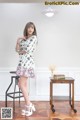 A woman standing in front of a white wall wearing a floral dress.