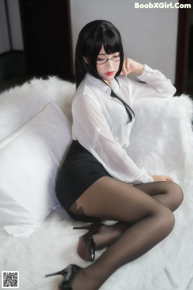 A woman in a white shirt and black skirt sitting on a white couch.